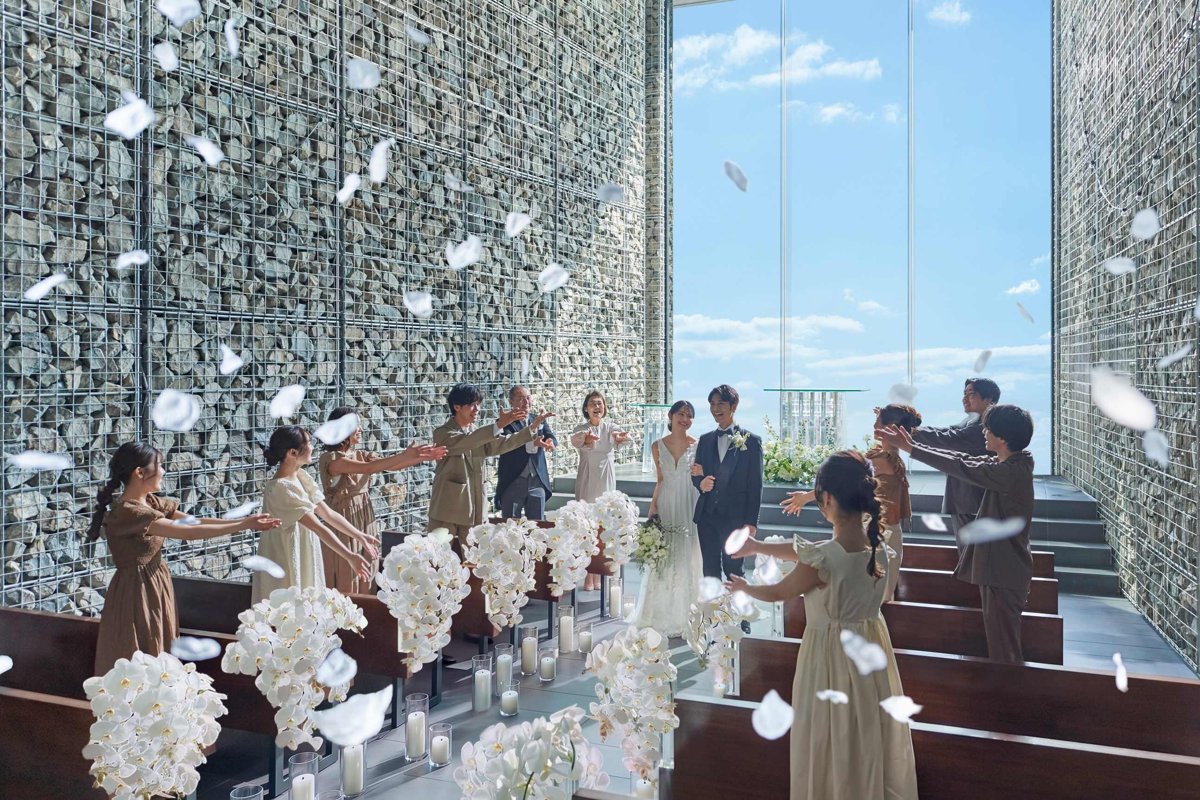 青空をのぞむ天空の教会で、フラワーシャワーに包まれる新郎新婦とゲスト